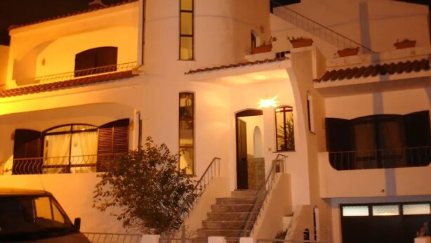 A two-story house with a balcony, a staircase, and a car parked in front.