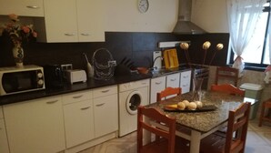 A compact kitchen with a microwave, toaster, and sink. There is a dining table with chairs and a vase with flowers.