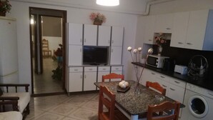 A compact kitchen with a dining table, chairs, a washing machine, and a TV.