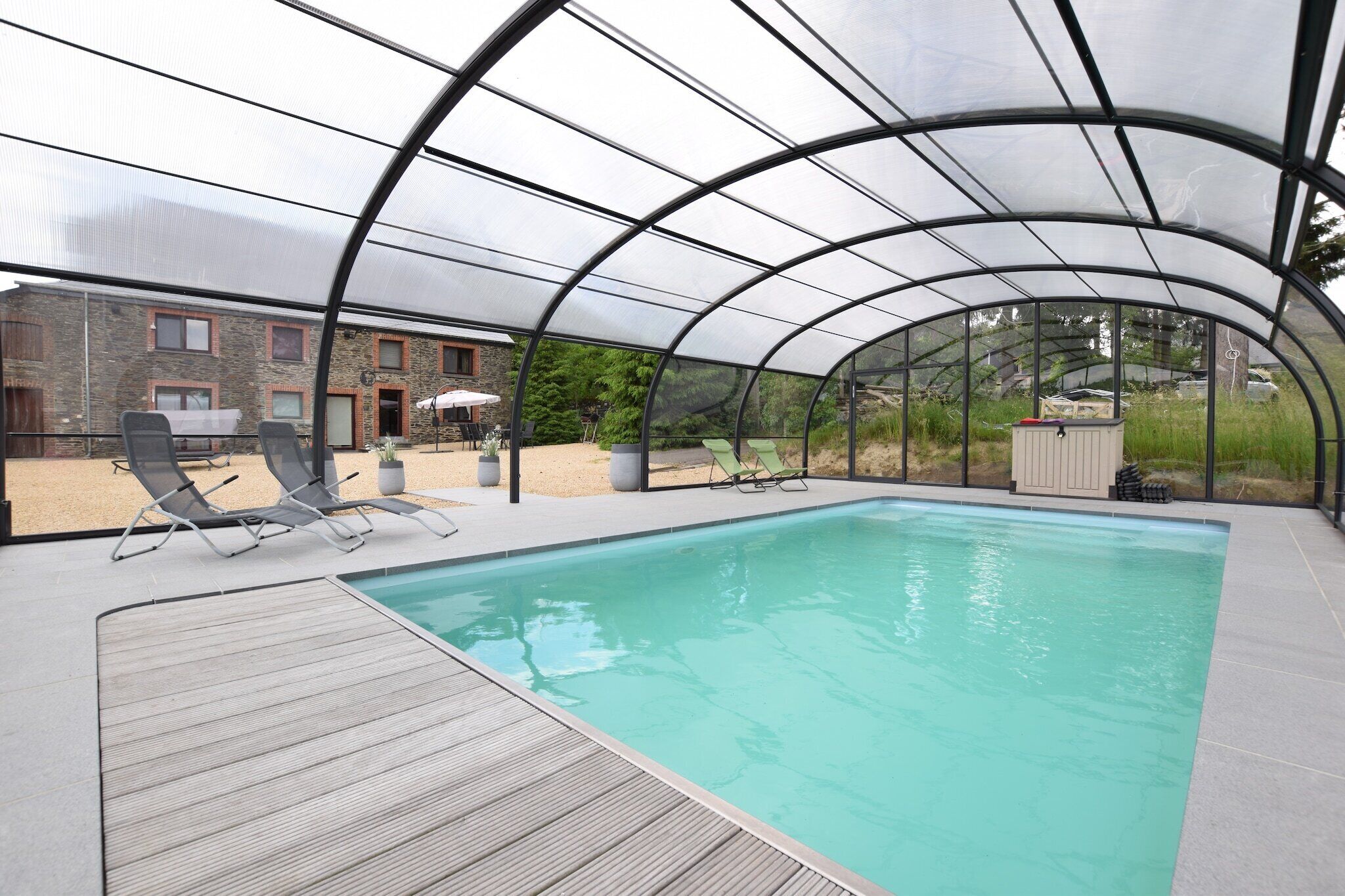 A covered swimming pool with lounge chairs and a stone building in the background.