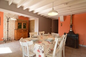 Comedor con una mesa dispuesta para cuatro, sillas blancas, un aparador de madera y una estufa antigua.