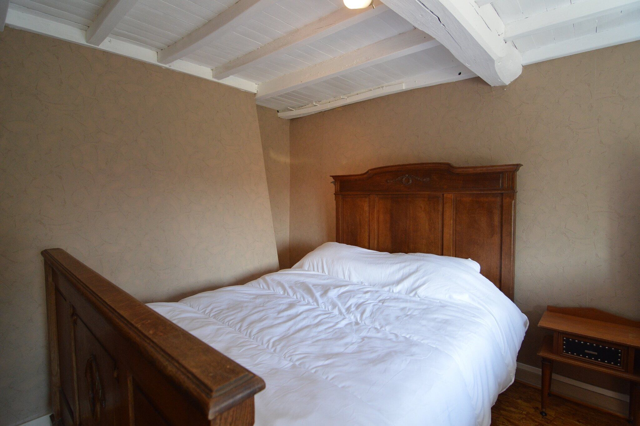 Een slaapkamer met een houten bed, een nachtkastje en een plafond met zichtbare balken.