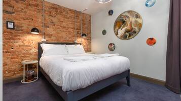 Une chambre moderne avec un mur en briques, un grand lit, deux lampes suspendues et des œuvres d’art abstraites accrochées au mur.