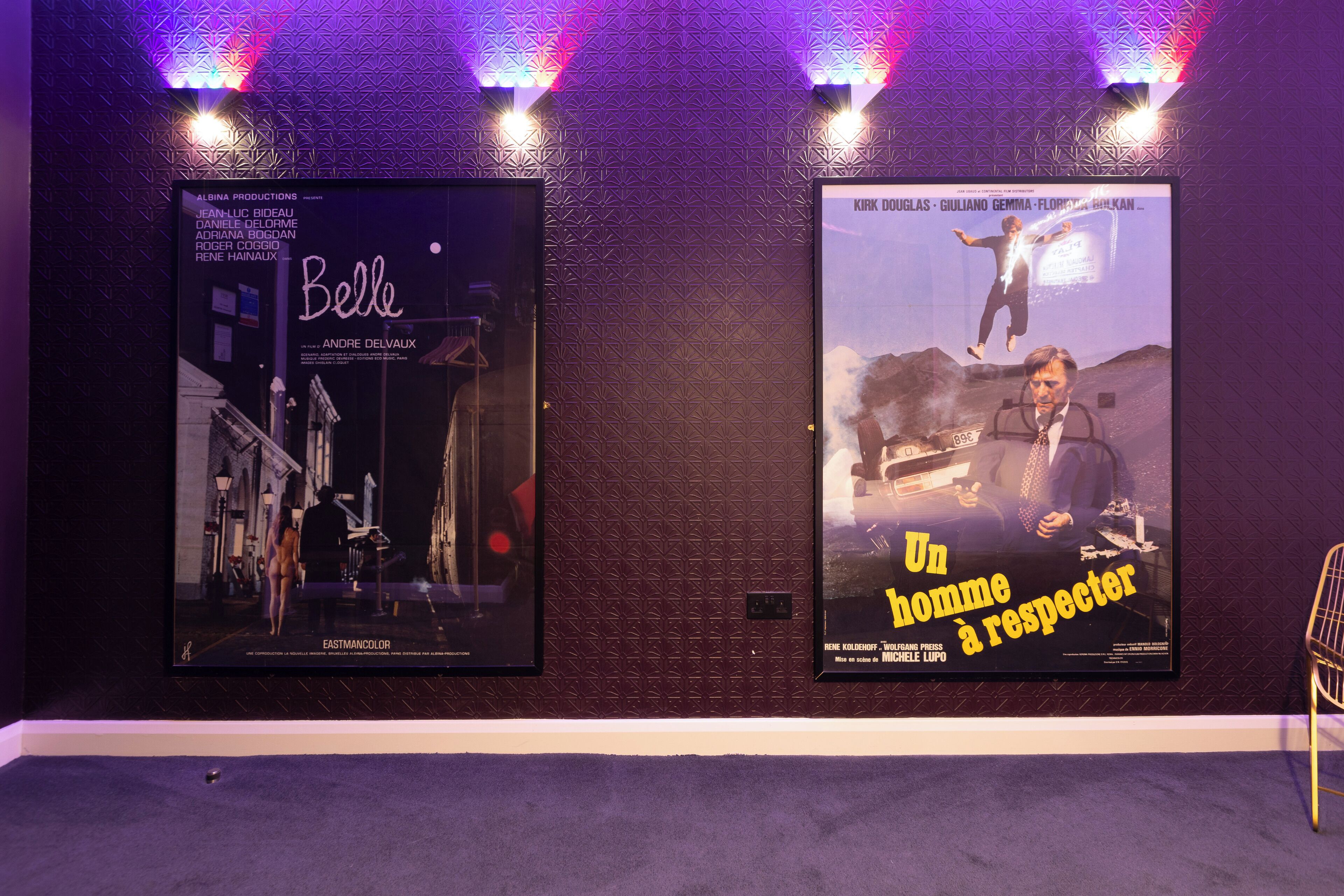 Two movie posters on a wall with patterned wallpaper and a carpeted floor.