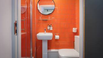 A bathroom with orange tiles, a white sink, a toilet, and a glass shower enclosure.