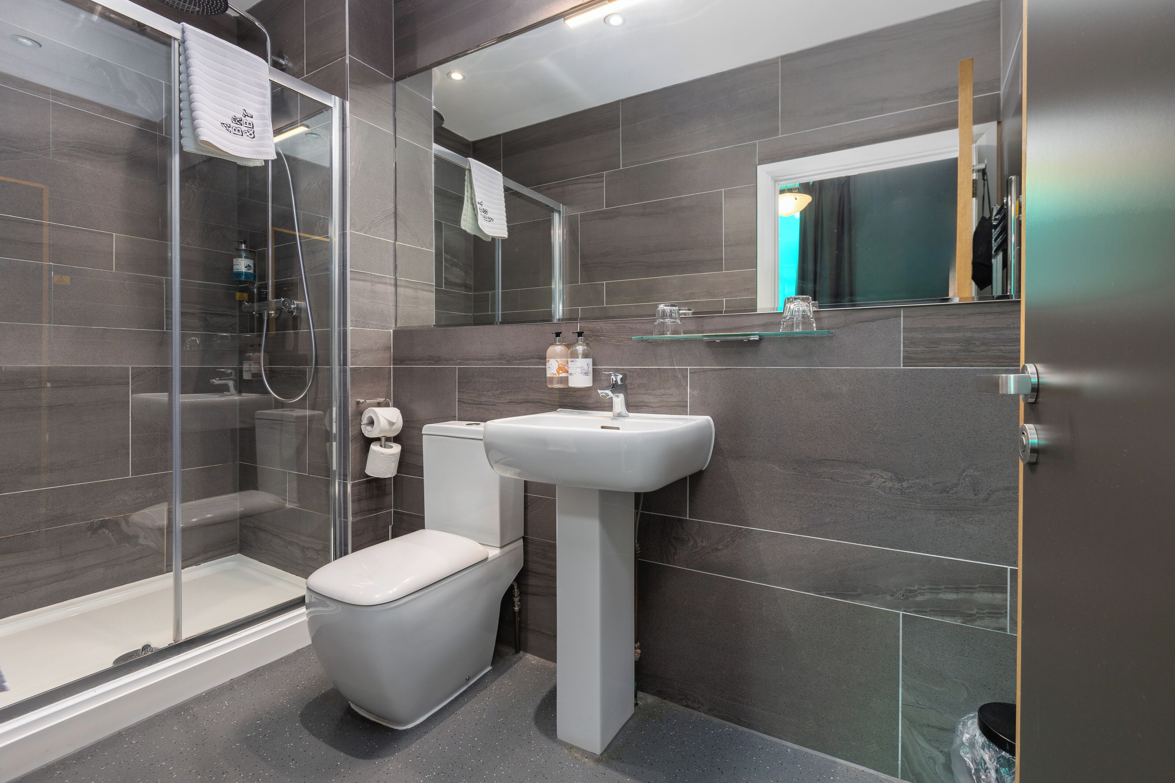 Un baño moderno con cabina de ducha de vidrio, un inodoro blanco y un lavabo sobrepedal.