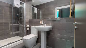 Un baño moderno con cabina de ducha de vidrio, un inodoro blanco y un lavabo sobrepedal.