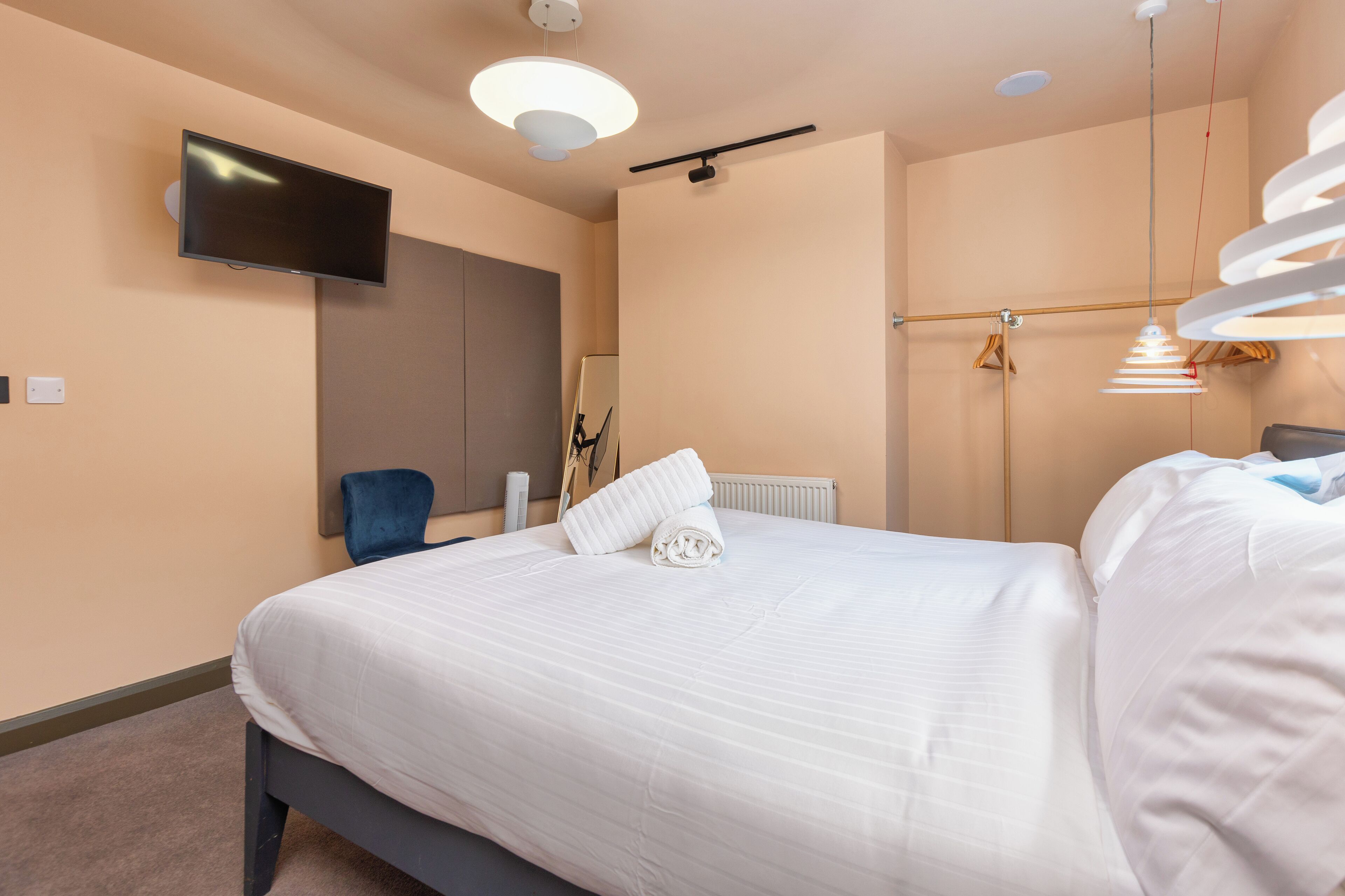 Ein modernes Hotelzimmer mit einem großen Bett, einem flachbildfernseher an der Wand und einer auffälligen Pendelleuchte.