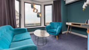A modern room with a large window, two blue armchairs, a small table, and a desk with drawers. - ART B&B (Blackpool)