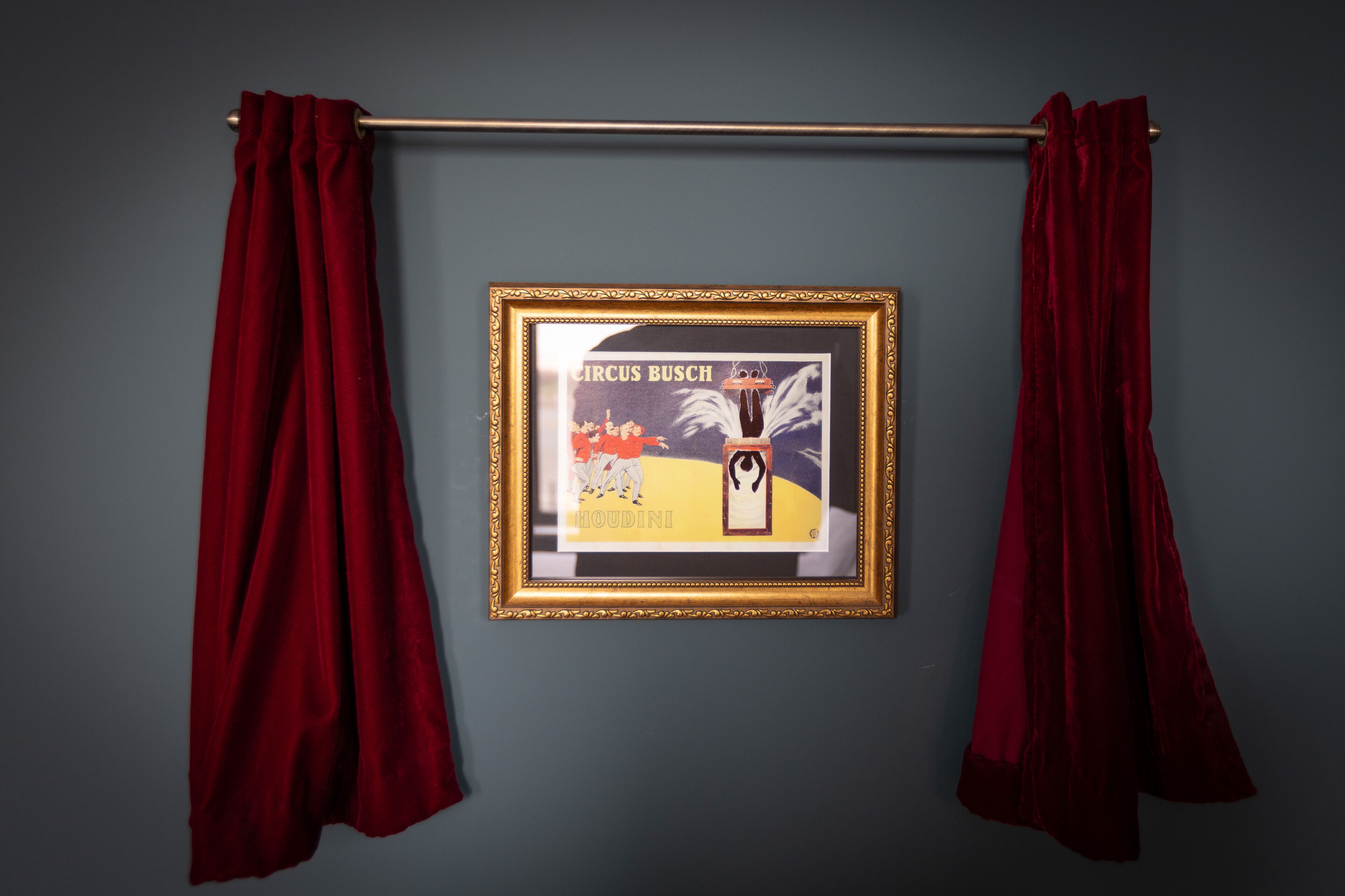 A framed poster on a wall with red curtains.