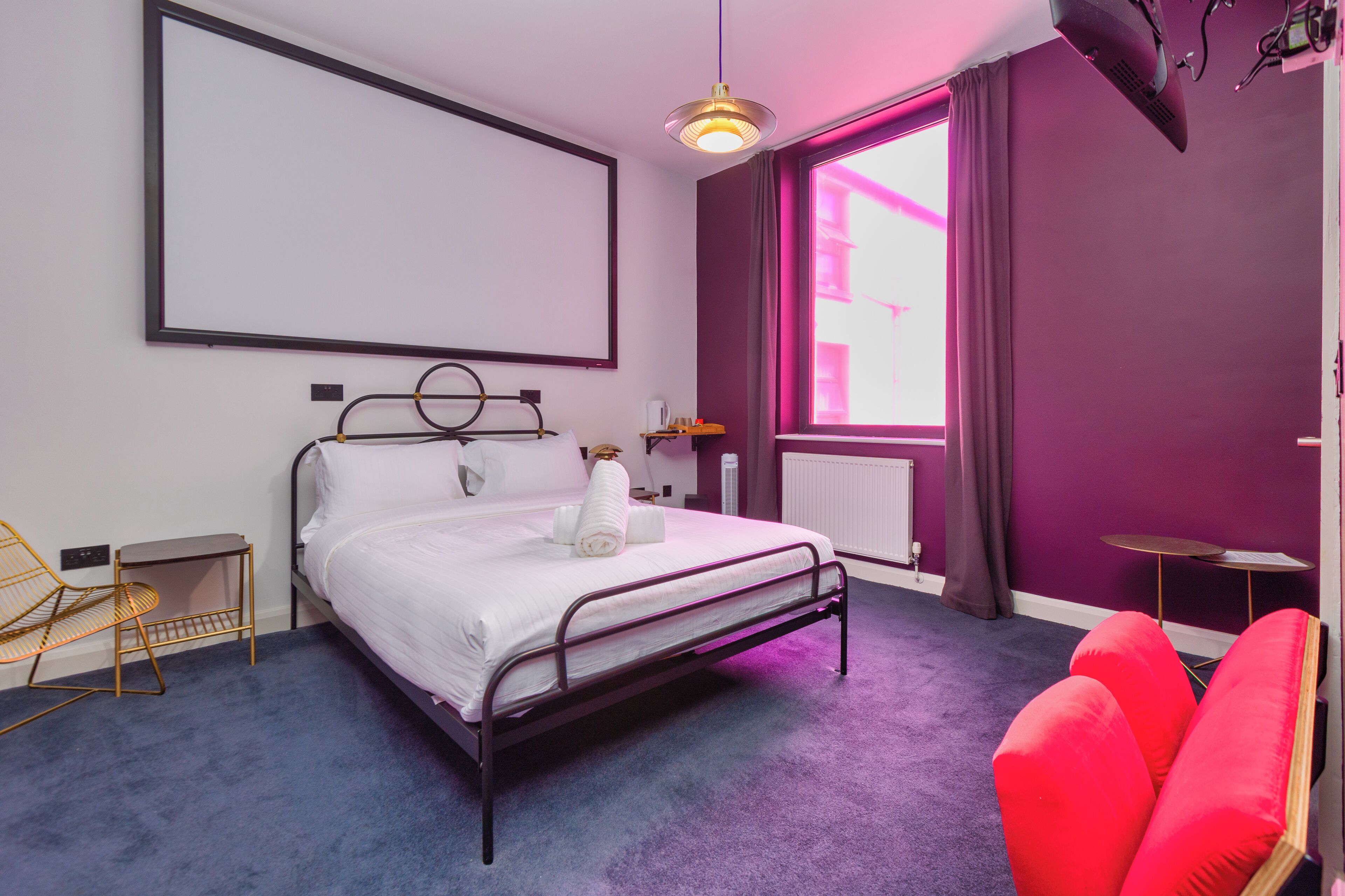 A bedroom with a bed, a chair, a table, and a window with curtains.