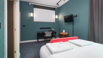 A hotel room with a bed, a desk, a chair, a TV, and a projector screen.