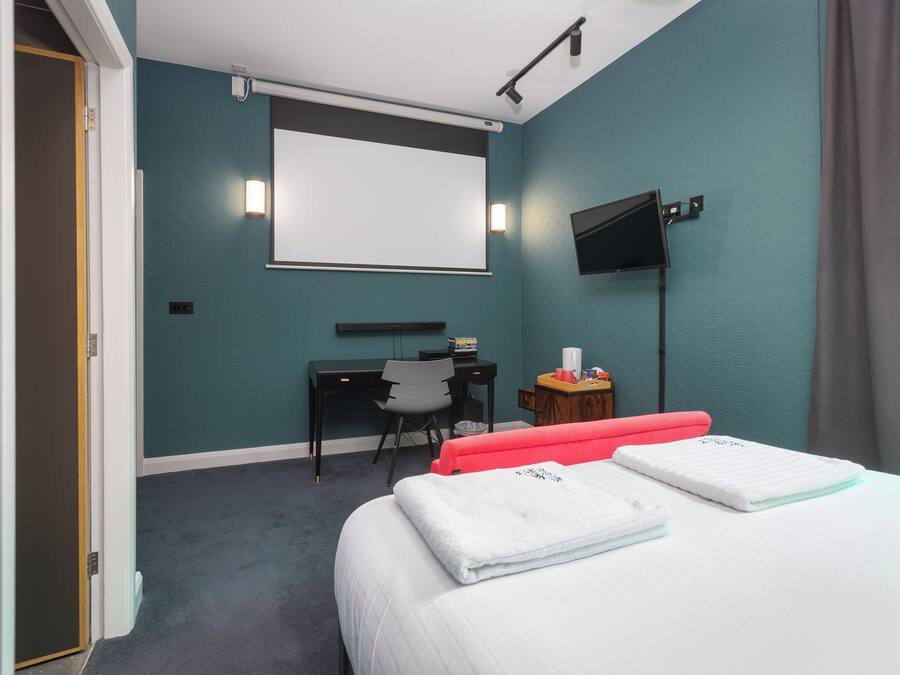 A hotel room with a bed, a desk, a chair, a TV, and a projector screen.