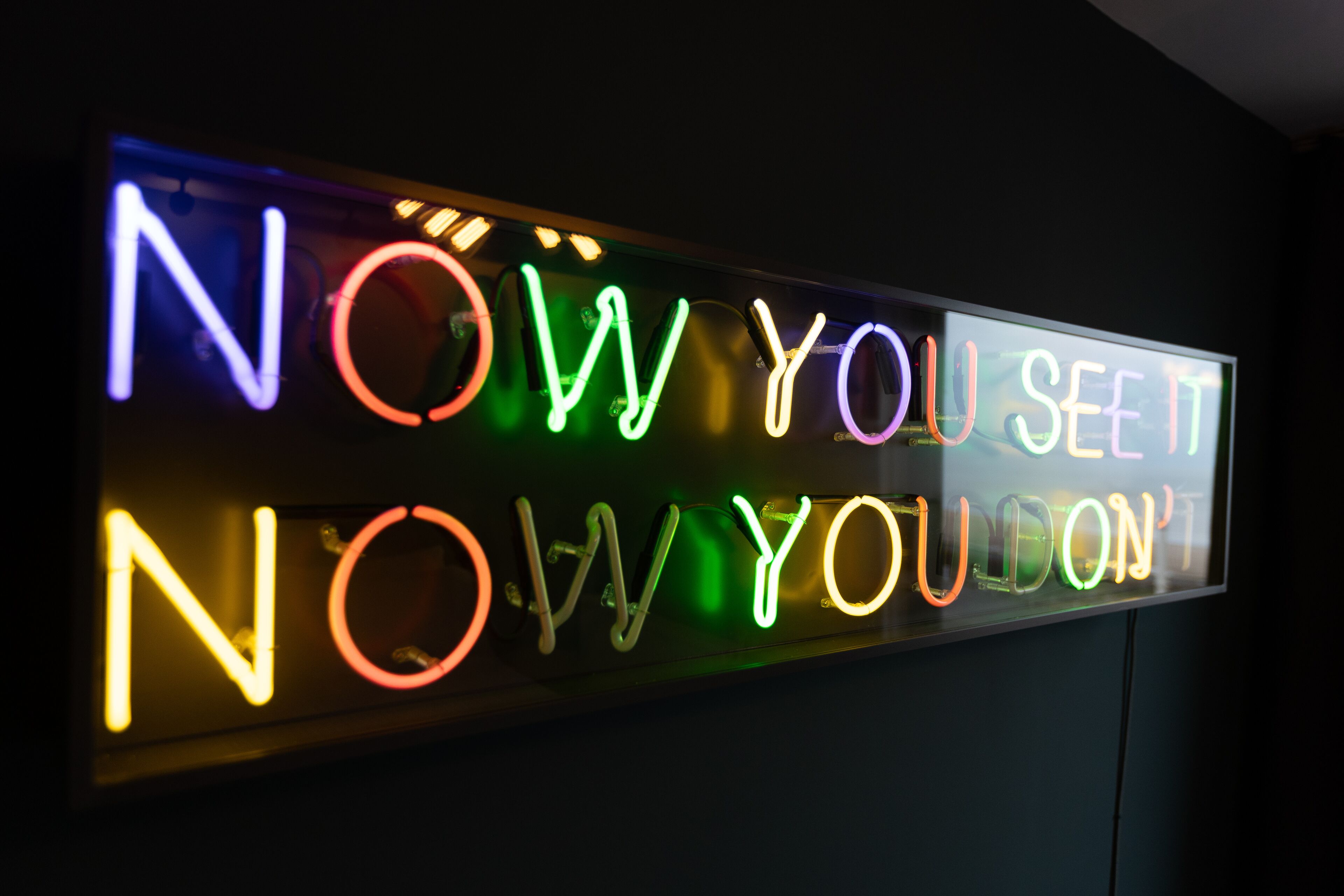 A neon sign with the text "NOW YOU SEE IT NOW YOU DON'T".