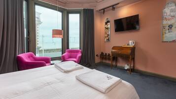Habitación de hotel con una cama grande, dos sillas rosadas, un escritorio de madera, una televisión y vistas a un edificio a través de la ventana.