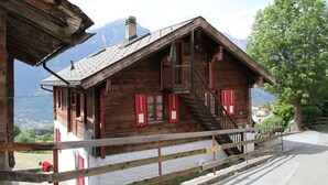 A wooden chalet with a steep roof, red shutters, and a wooden staircase leading to the entrance. - Boutique Apartment in Valais with Balcony (Guttet-Feschel)