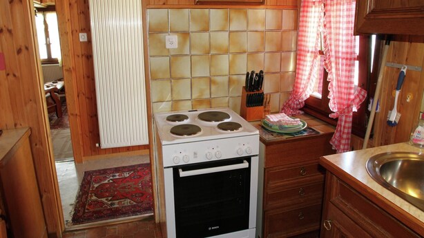 A kitchen with a Bosch stove, wooden cabinets, a tiled backsplash, and a red and white checkered curtain.