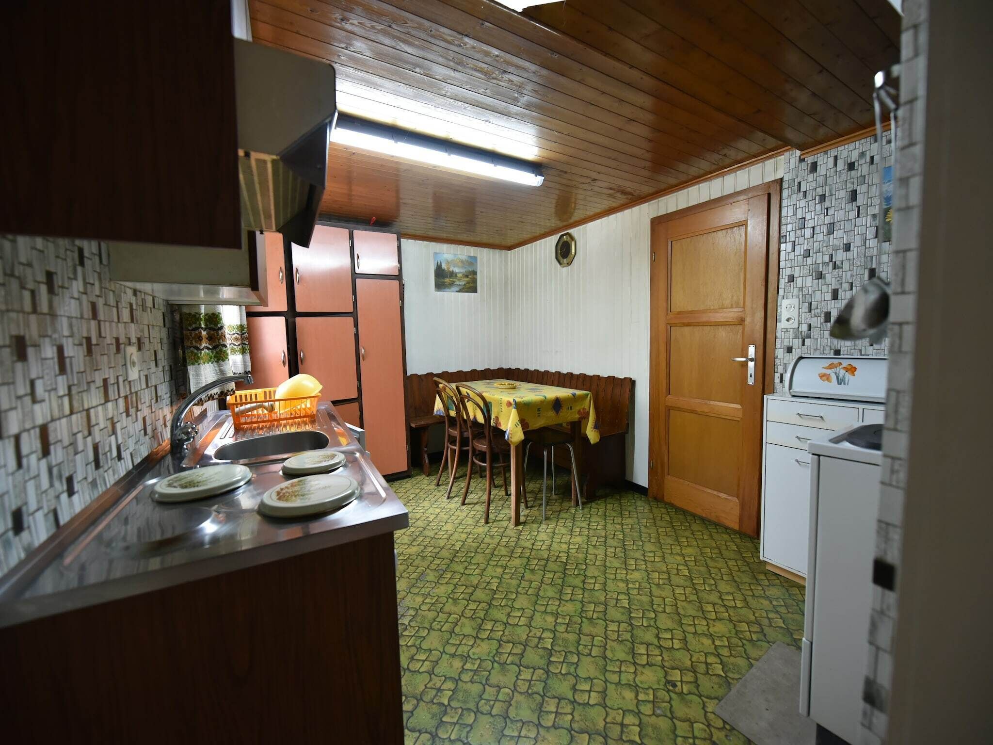 A compact kitchen with a dining area, wooden cabinets, a tiled backsplash, and a patterned floor.