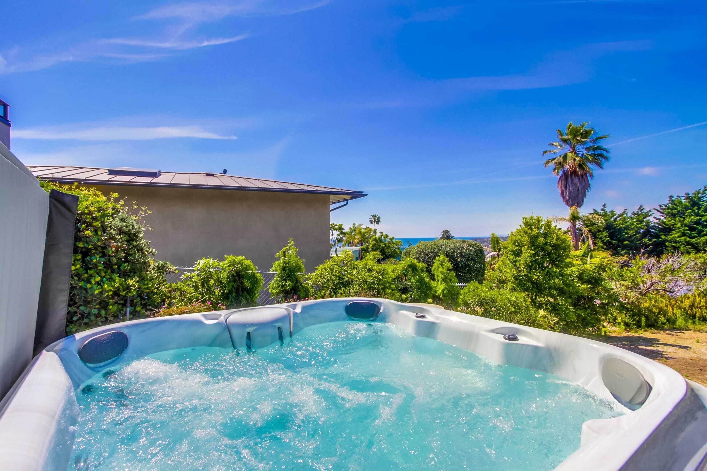 Ein Whirlpool in einem Garten mit einem Haus und Palmen im Hintergrund.