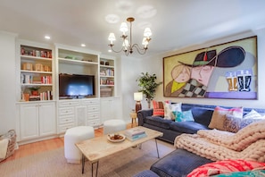 A modern living room with a television, bookshelves, a sofa, and a coffee table. - Solana Beach House w/ Hot Tub & Ocean Views (Solana Beach)