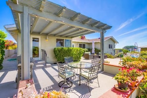 A covered patio with a glass table and chairs, surrounded by potted plants and a pergola.
