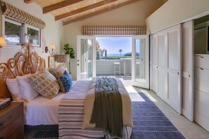 A bedroom with a bed, bedside tables, a nightstand, a window with curtains, a view of the outdoors, and a sliding door leading to a balcony.