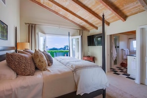 Quarto com cama grande, TV e varanda com vista.