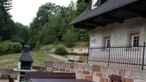 Un patio exterior con paredes de piedra, una parrilla de barbacoa y bancos de madera.