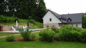 Una casa con piscina, rodeada de vegetación y un muro de piedra.