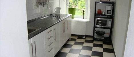 A kitchen with white cabinets, a black and white checkered floor, a window with a view of greenery, and a coffee machine.