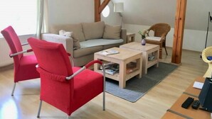 Un soggiorno con un divano, una poltrona rossa, un tavolino in legno e una sedia in vimini.
