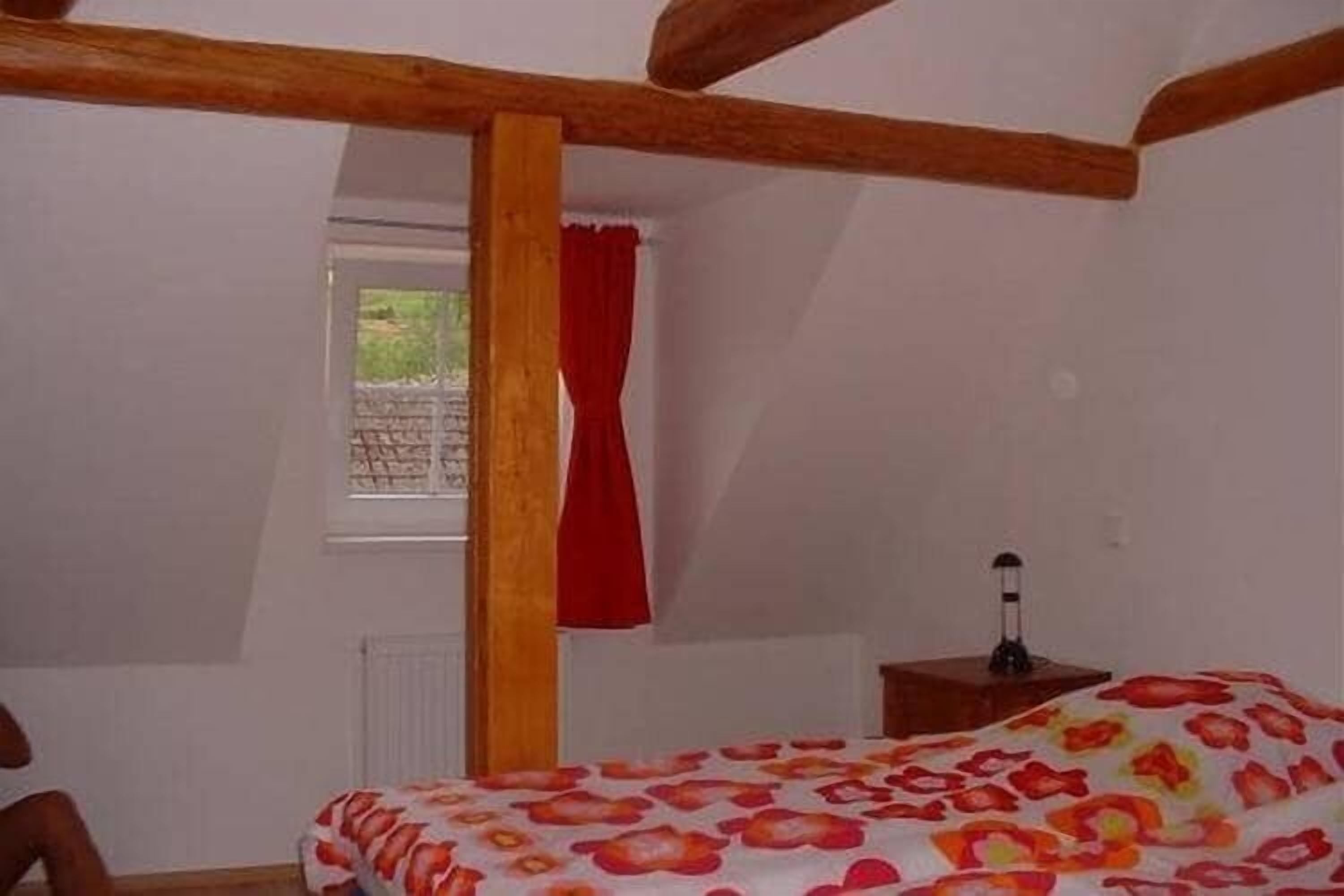 Ein Schlafzimmer mit einem Bett, einem Fenster mit rotem Vorhang und einem Nachttisch mit Lampe.