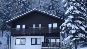 A two-story building with a balcony on the upper floor, surrounded by snow-covered trees.