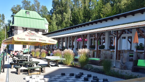 An outdoor seating area with tables and chairs, surrounded by potted plants and a checkered floor pattern.