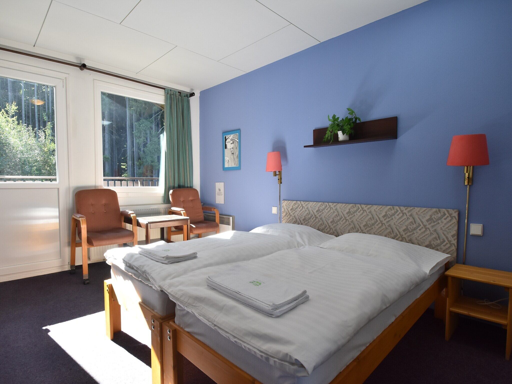 A hotel room with a bed, two chairs, a desk, a lamp, and a window with curtains.