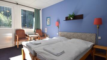 A hotel room with a bed, two chairs, a desk, a lamp, and a window with curtains.