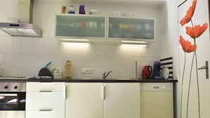 A kitchen with white cabinets, a stove, a dishwasher, and a microwave. There are two glass-fronted cabinets above the counter with various kitchen items.