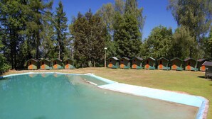 A swimming pool with a surrounding deck, surrounded by small cabins with orange doors and green roofs.