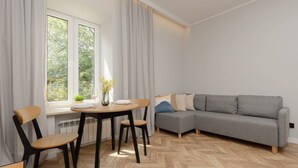 A modern living room with a grey sofa, wooden herringbone floor, and a dining area with a table and chairs.