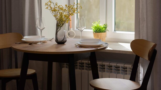 A dining table with two chairs, a vase with yellow flowers, and two wine glasses on a window sill.