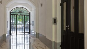 A hallway with a marble floor, a black door, and an arched entrance leading to a gate.