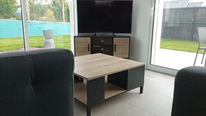 A modern living room with a TV, a wooden coffee table, and two grey armchairs. - Maison Neuve de 2023, Plain Pied, 2 Chambres, à 10 Minutes à Pied de la Plage (Fréhel)