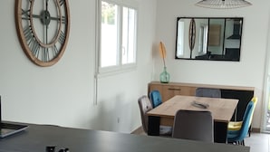A modern kitchen with a central island, a dining area with a wooden table and chairs, and a large wall clock. - Maison Neuve de 2023, Plain Pied, 2 Chambres, à 10 Minutes à Pied de la Plage (Fréhel)