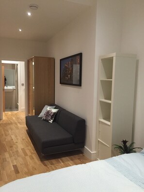 A modern, well-lit room with a dark-colored sofa, a white bed, and a wooden wardrobe.