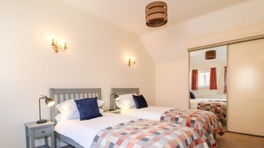 A bedroom with two beds, a nightstand with a lamp, a mirror, and a ceiling light fixture.