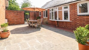 A patio with a table and chairs, a brick wall, and a window with a white frame.