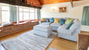 A cozy living room with a grey sofa set, a brick fireplace, and a large window with curtains.