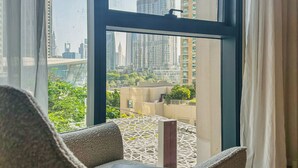 A modern room with a large window offering a view of high-rise buildings and greenery. - Maison Privee - Luxury 2Bedroom w/ Burj Khalifa & Fountain Views (Dubai)