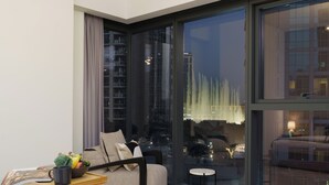 A modern living room with a sofa, a small table with a bowl of fruit, and a view of a cityscape through large windows. - Maison Privee - Luxury 2Bedroom w/ Burj Khalifa & Fountain Views (Dubai)