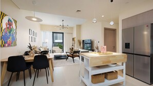 A modern kitchen with a large refrigerator, a dining area with a wooden table and chairs, and a living room with a sofa and a TV. - Maison Privee - Luxury 2Bedroom w/ Burj Khalifa & Fountain Views (Dubai)